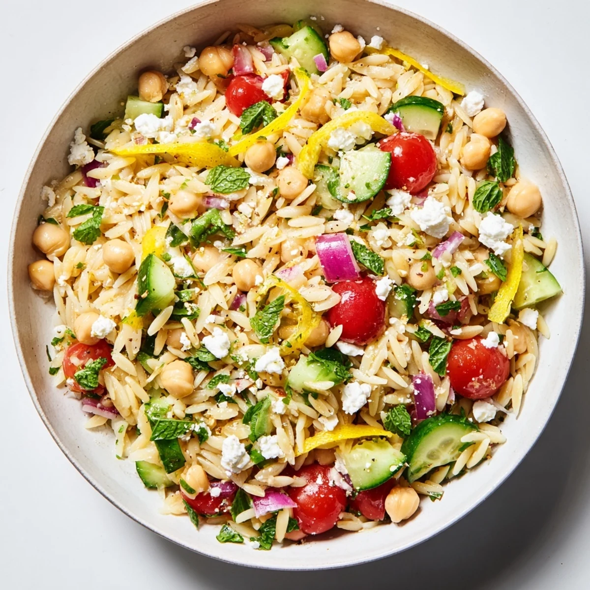 Bright and fresh Lemony Chickpea Orzo Salad with diced cucumber, cherry tomatoes, and crumbled feta on a wooden serving board.  