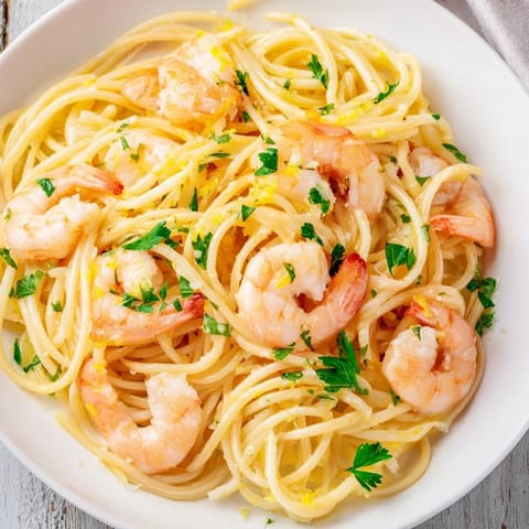 Juicy lemon garlic shrimp pasta served in a warm bowl, featuring plump shrimp and a silky, herb-flecked sauce.  