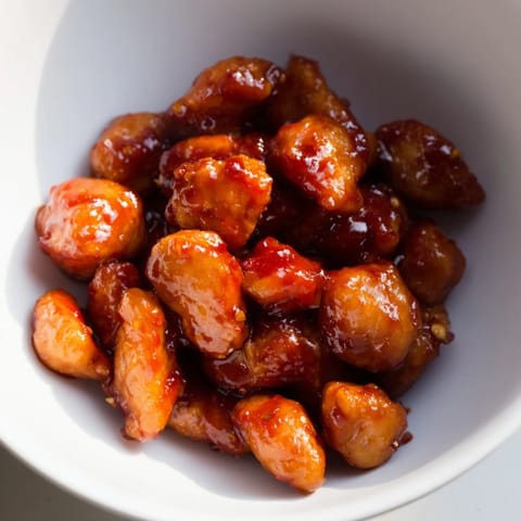 A close-up of sweet chili chicken bowl, featuring glossy sauce-drenched chicken, white jasmine rice, and vibrant green steamed broccoli.