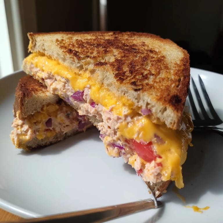 A spicy tuna melt sandwich with cheddar cheese and tomato slices, served hot on a rustic wooden plate.