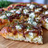 A golden flatbread topped with sweet caramelized onions, creamy goat cheese, and fresh thyme for a Mediterranean-inspired appetizer.